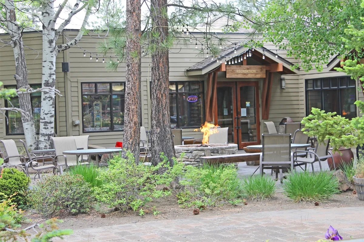 An inviting outdoor area featuring a fire pit, entrance door, comfortable seating, and surrounding trees. The space suggests communal relaxation and outdoor gatherings, all within a natural setting.