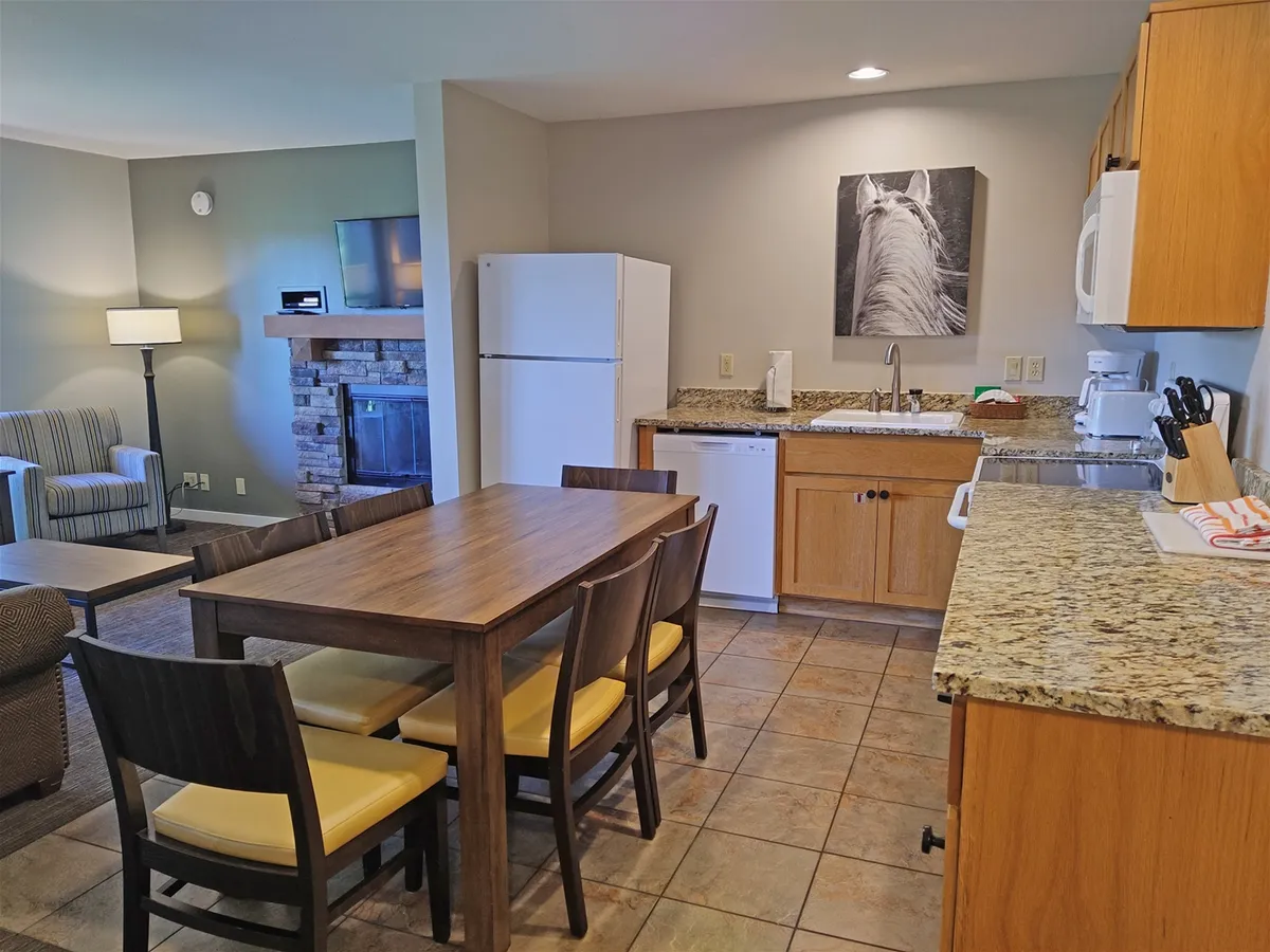 An inviting interior scene featuring a dining table, kitchen counter, fireplace, and artwork, evoking a cozy, communal space within the condo where families and friends gather after a day of resort adventures.