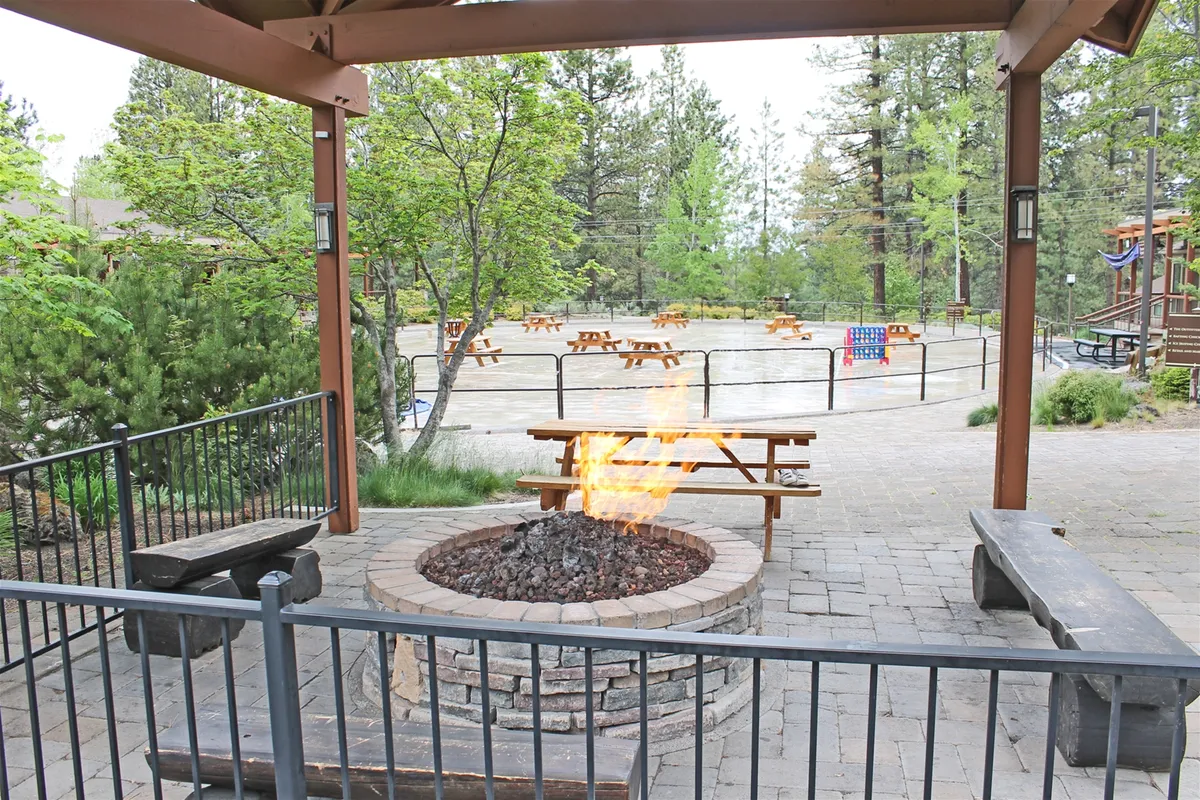 An inviting fire pit area encircled by wooden benches and shaded by tall trees. The communal setup invites groups to gather around the fire, enjoy evening conversations, and participate in outdoor games or storytelling under the stars.