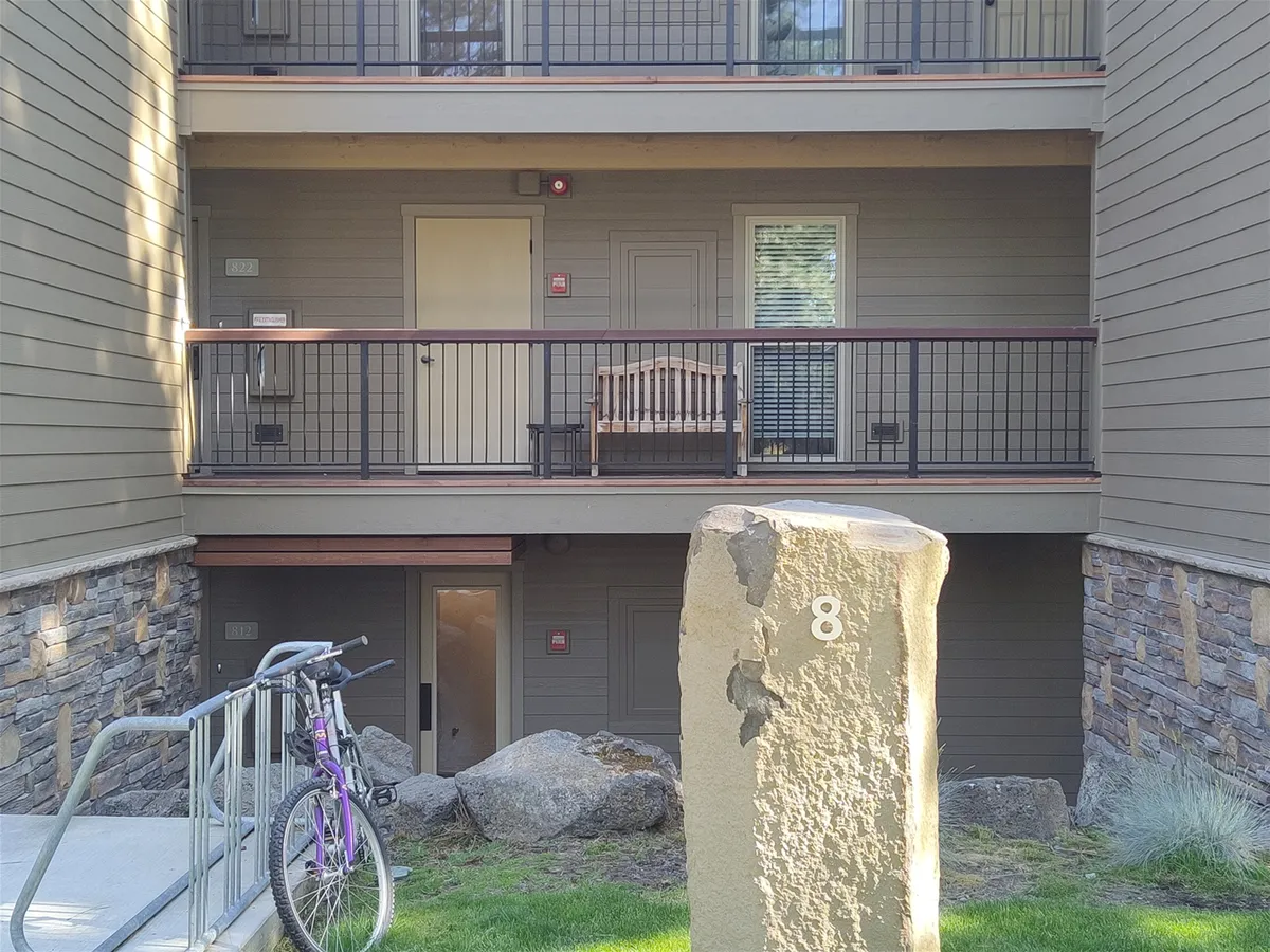 A welcoming front porch features a comfortable bench and a stone marker, with a bicycle parked nearby. The setting is surrounded by greenery, conveying a sense of adventure and relaxation before or after a day outdoors.