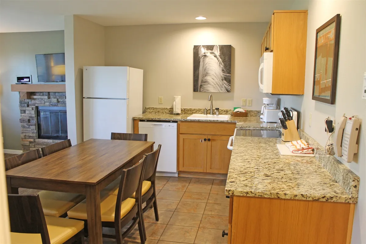 A dining table set adjacent to a modern kitchen, framed by inviting artwork on the wall. The atmosphere is welcoming and ideal for shared meals or casual cooking, reinforcing the convenience and home-like comfort described in the section.