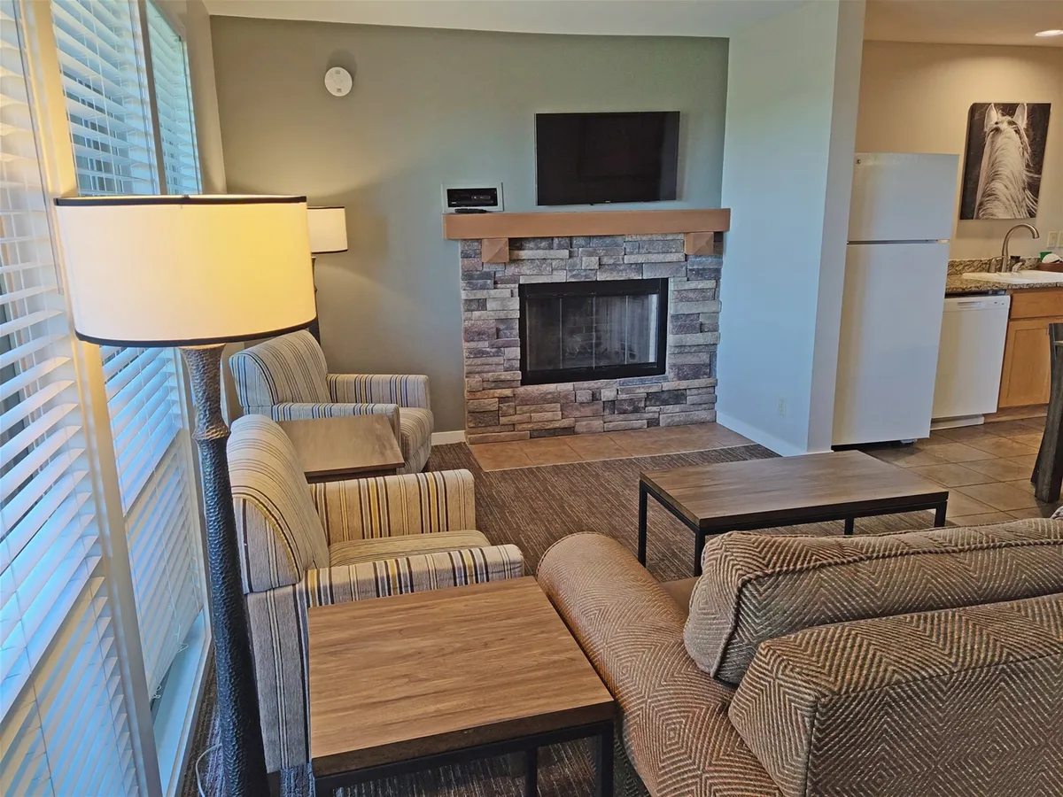 An open-concept living area featuring a cozy seating arrangement anchored by a fireplace, with a television visible and the kitchen area in the background. The scene feels both inviting and contemporary, perfect for socializing or unwinding after a day outdoors.